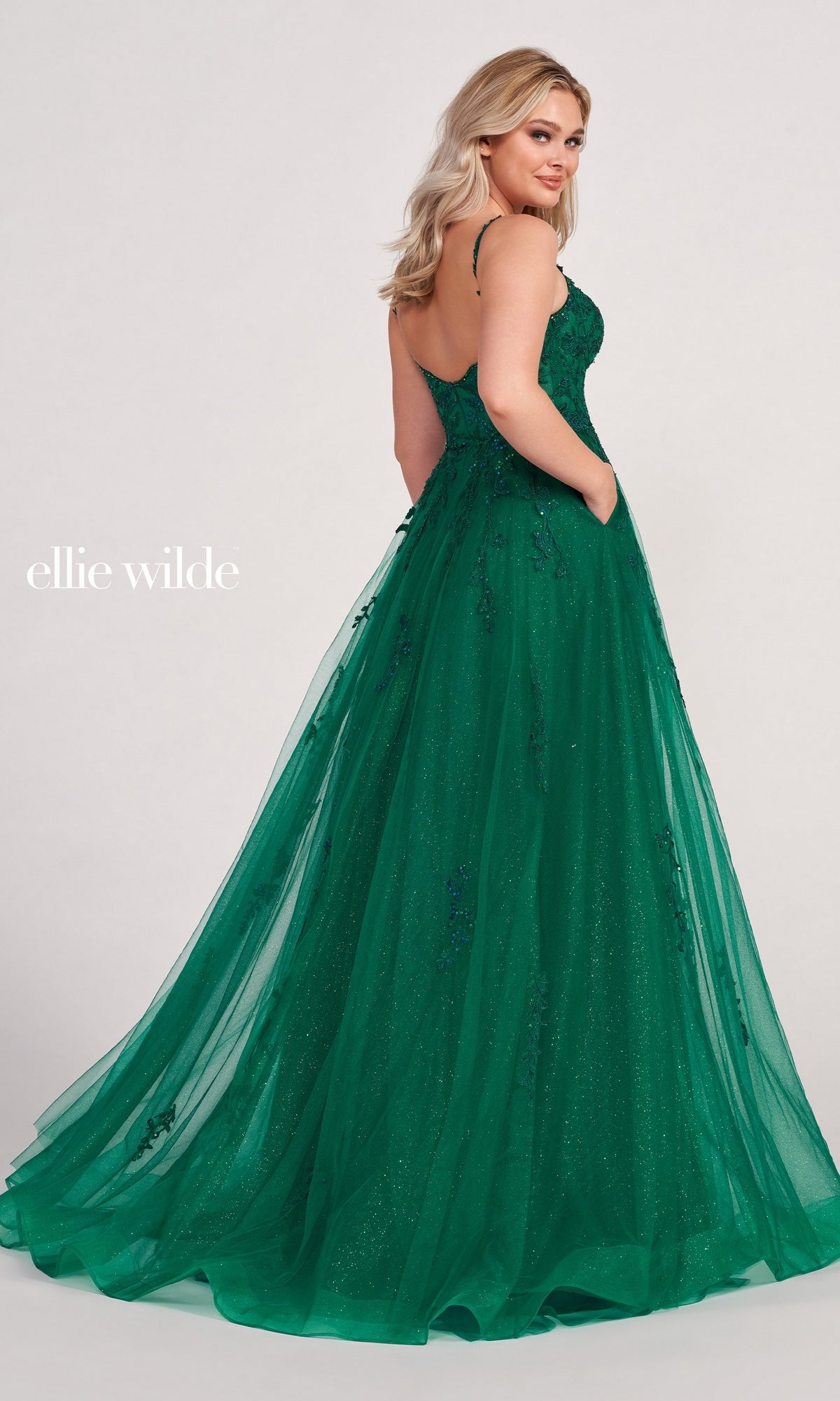 A woman faces away, glancing over her shoulder in the Ellie Wilde Long Glitter-Tulle A-Line Formal Dress, featuring a flared skirt, subtle embellishments, delicate tulle overlay, and elegant embroidered floral appliques.